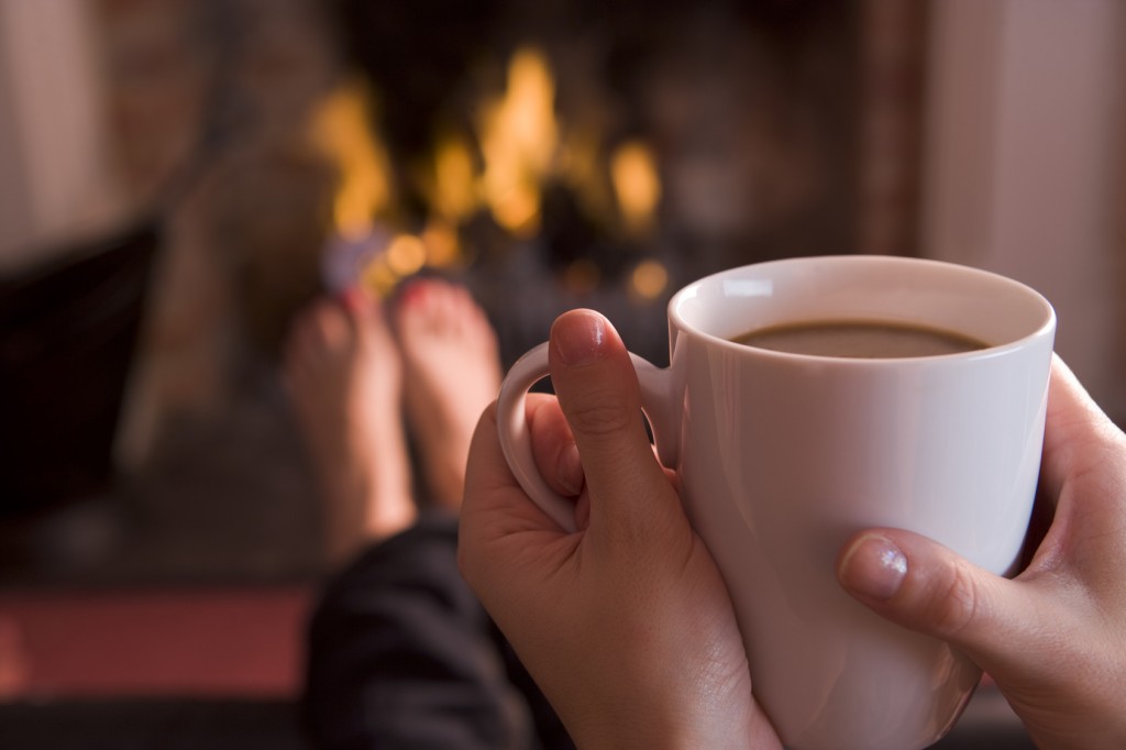 Feet warming at a fireplace with hands holding coffee